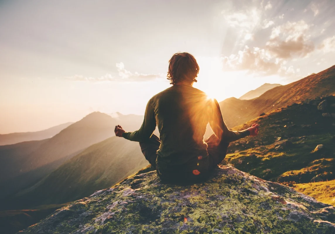 Person meditating on mountain at sunset.